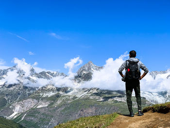 Rear view of man looking at mountains against blue sky