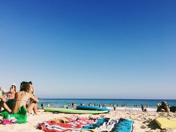 People at beach against clear blue sky