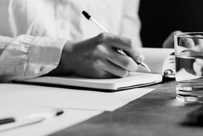 Midsection of man writing on book at table