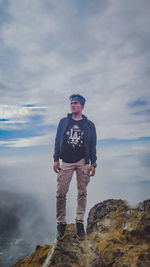 Man standing on rock against sky