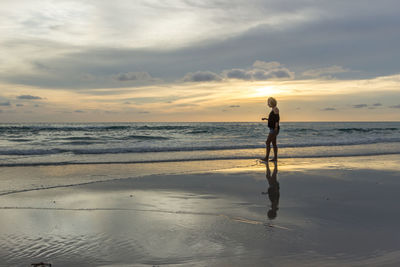 Woman standing on beach against sky during sunset