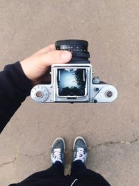 High angle view of man holding camera with reflection of tree in