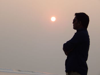 Side view of thoughtful man standing at beach during sunset