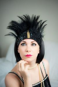 Beautiful woman wearing jewelry and headband looking away while sitting on bed against wall