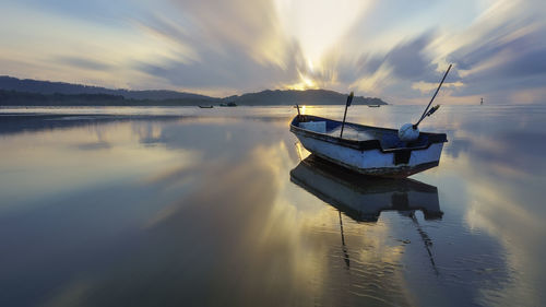 Empty fishing boat moored at lake during sunset