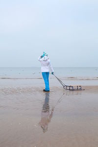 Reflection of woman with sledge standing at beach during winter