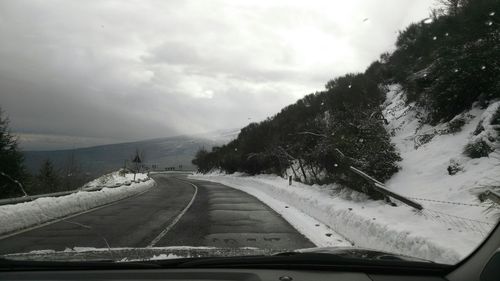 Road amidst trees against sky seen through car windshield