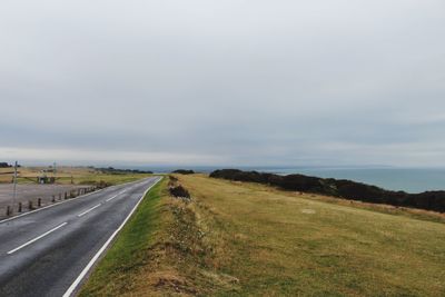 Empty road amidst field against sky