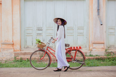 Portrait of young woman with bicycle standing against wall