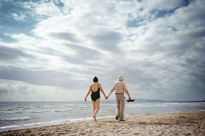 Rear view of couple on beach against sky