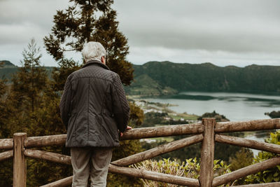 Rear view of man looking at lake against sky