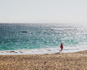 Person walking on shore at beach against clear sky during sunny day