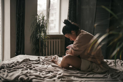 Side view of young man sitting on bed at home