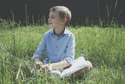 Boy with book sitting on field