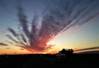 Cars on road against dramatic sky during sunset