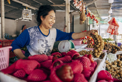 Smiling female vendor picking up bunch of longan at market stall