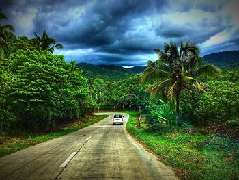 Road amidst trees against cloudy sky