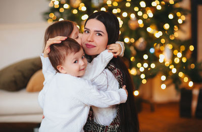 Portrait of girl standing against illuminated string lights at home