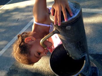 High angle view of girl drinking water from drinking fountain on street