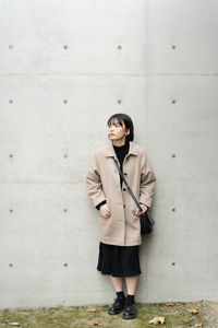 Portrait of young woman standing against wall