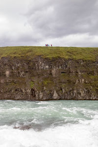 Hill by river against cloudy sky