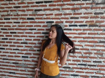 Young woman standing against brick wall