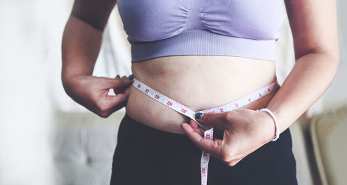 Midsection of woman measuring abdomen