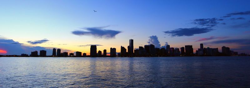 Panoramic view of silhouette city skyline by sea against sky