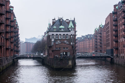 Bridge over canal amidst buildings in city against clear sky