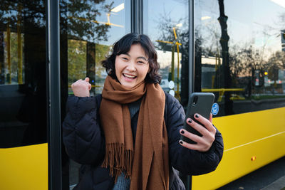 Portrait of young woman using mobile phone while standing in train