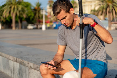 Young latin man with crutches using mobile phone after doing exercise