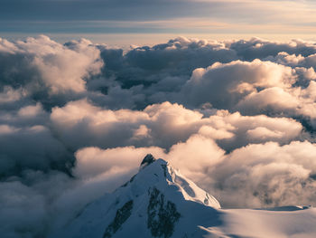 Aerial view of snowcapped mountains against cloudy sky during sunset