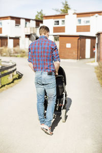 Rear view of man with baby carriage walking on sunny street