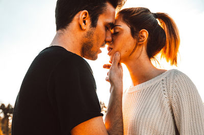 Side view of young couple kissing while standing against clear sky