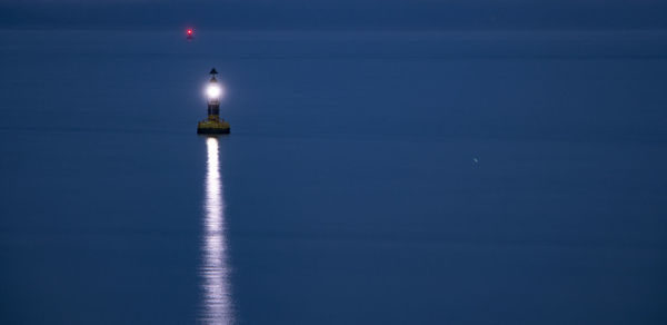 Lighthouse by sea against blue sky