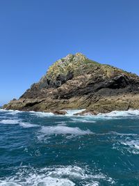 Rocks by sea against clear blue sky