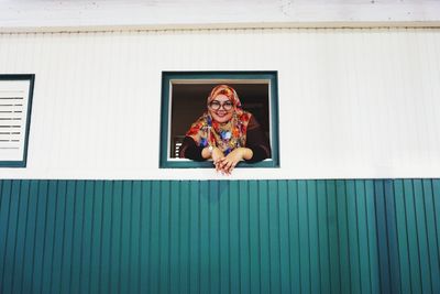 Low angle portrait of smiling young woman peeking window