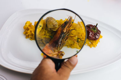 Close-up of cropped hand holding magnifying glass on seafood and rice served on plate