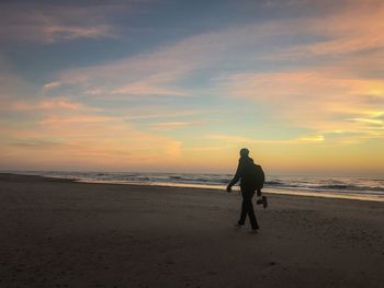 Rear view of woman on beach against sky during sunset