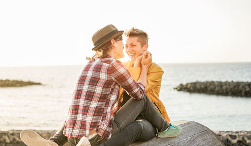 Cheerful lesbian couple sitting against sea during sunset