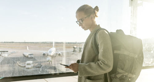 Side view of young woman using mobile phone against window