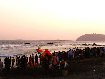 People on beach against clear sky during sunset