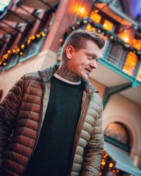 Young man looking away while standing in illuminated winter