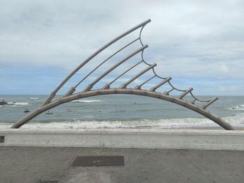 Metallic structure on beach against sky