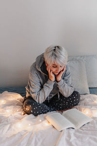 Woman sitting on bed while reading book at home