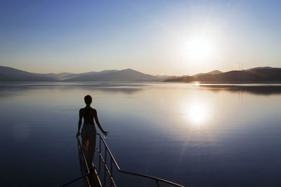 Silhouette man by lake against sky during sunset