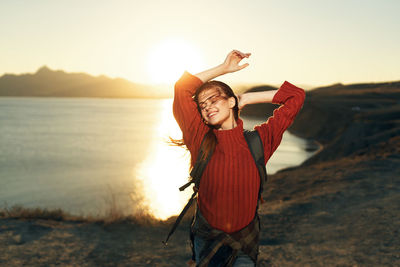 Woman standing with arms raised against sky during sunset