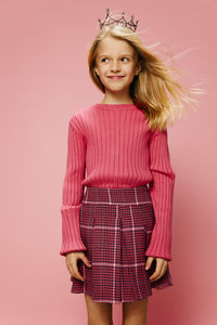 Portrait of young woman standing against pink background