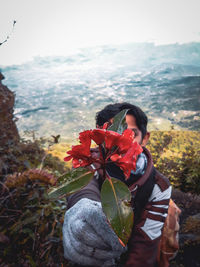 Man holding flower while standing against landscape