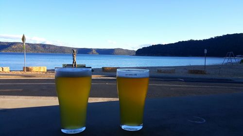 Close-up of beer on table by sea against clear sky